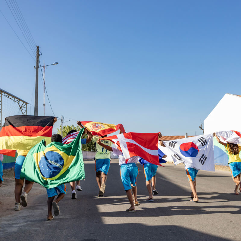 Children running and carrying a variety of country flags over their shoulders
