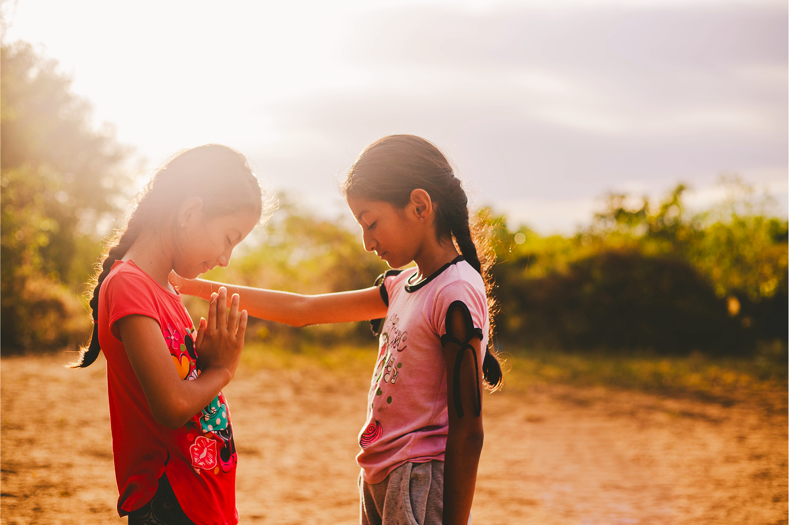 A girl putting her hand on another girl's shoulder and praying for her.