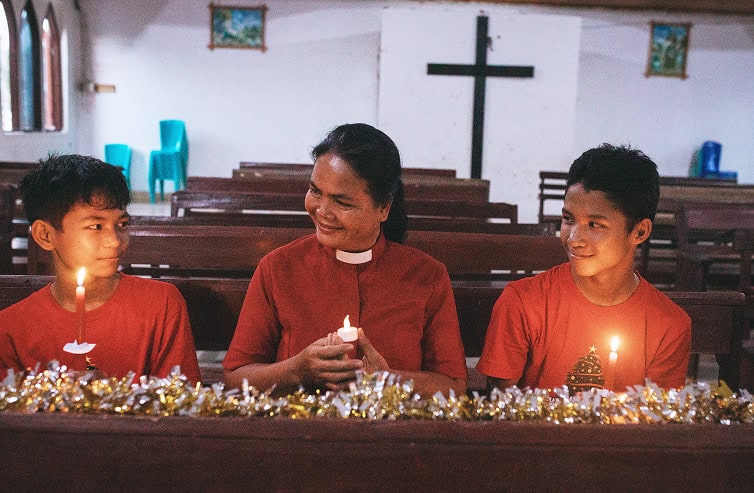 Two children and a pastor holding a candle on their hands. Looking at each other smiling.