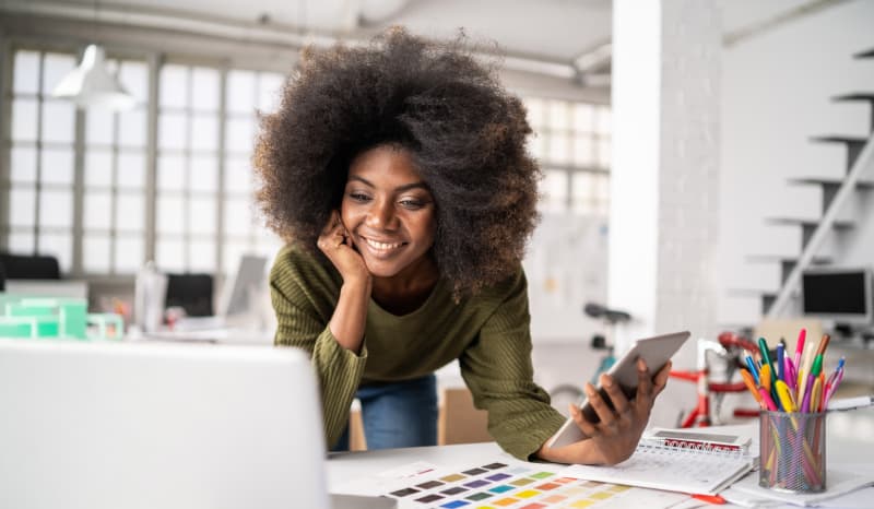 Young woman holding tablet looking at computer.