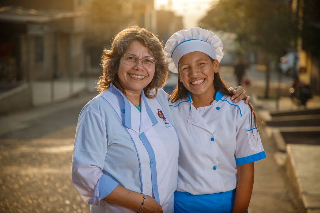 A woman stands outside with her arm around a girl wearing a chef's hat