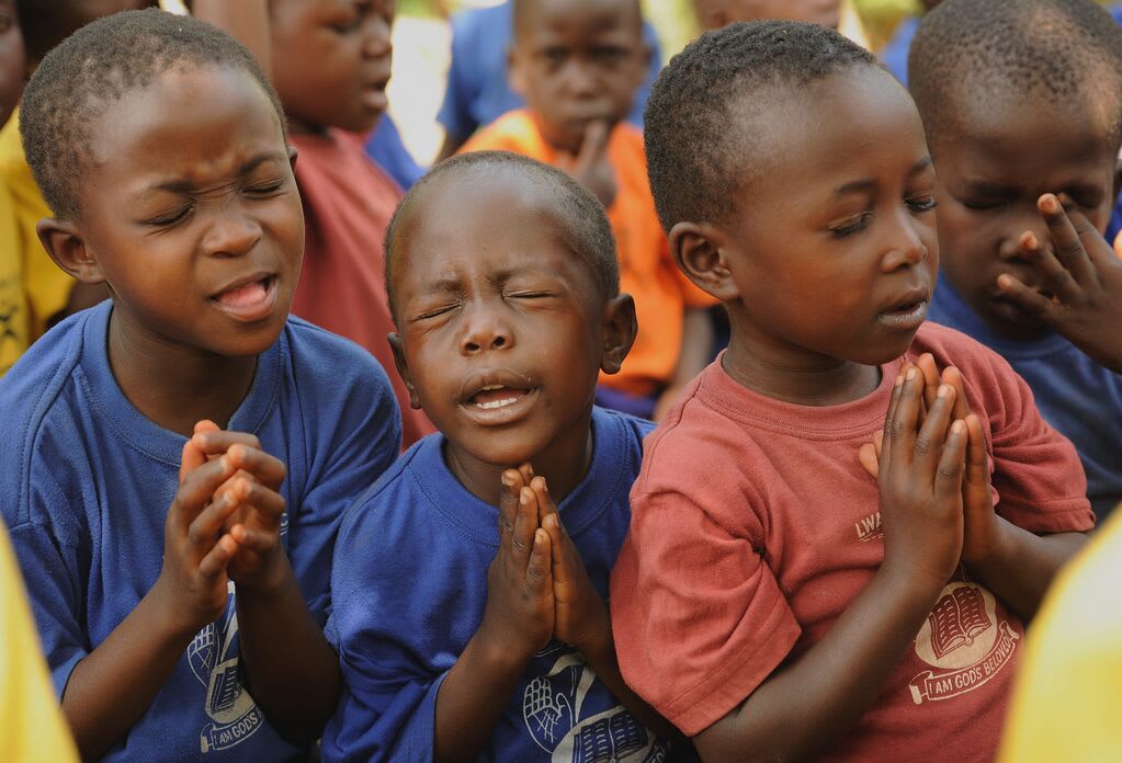 3 boys praying, one is squeezing his eyes closed very tightly