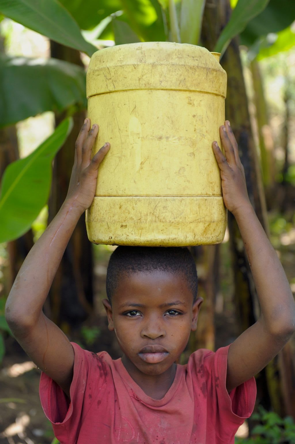 A young black boy holds a yellow water container on his head