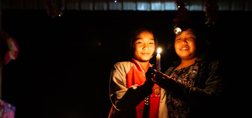 Two girls stand in candlelight.