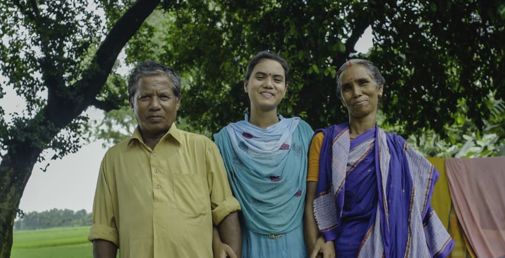 A Sri-Lankan family made up of the mom, dad and daughter standing together smiling
