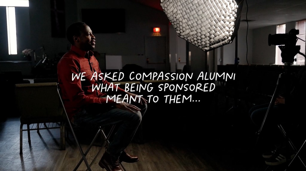 Martin, a Compassion alumnus from Uganda, sits in a video shoot environment. Text on the image says "We asked Compassion alumni what being sponsored meant to them..."
