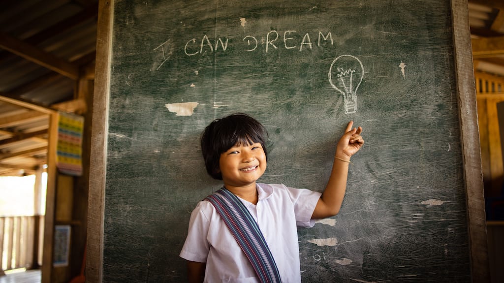 Little girl points to a black board with words that say "I can dream".