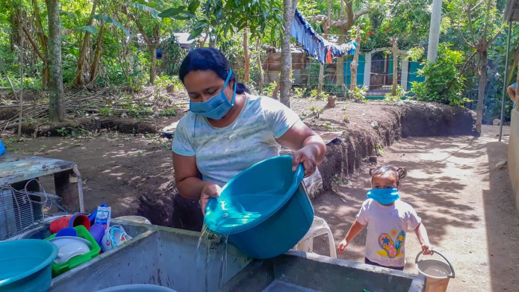 Yesenia fills up her sink with water from the water tank truck. Her daughter, Raquelita, follows behind with a bucket of water.