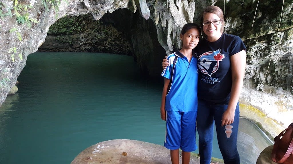 A woman and a teenage girl pose together in front of a pond in the mouth of a cave.