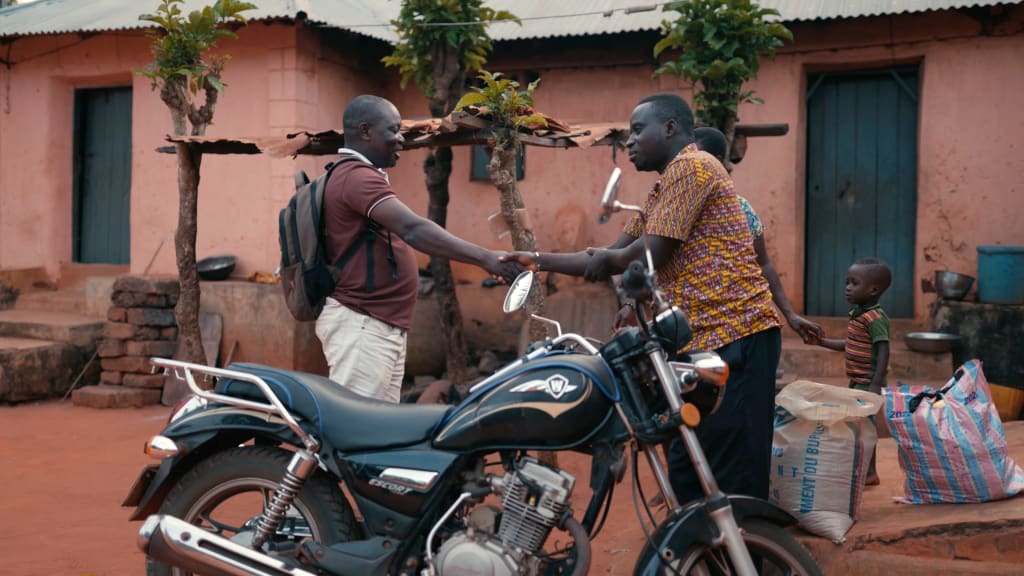 Two men shake hands behind a motorbike.