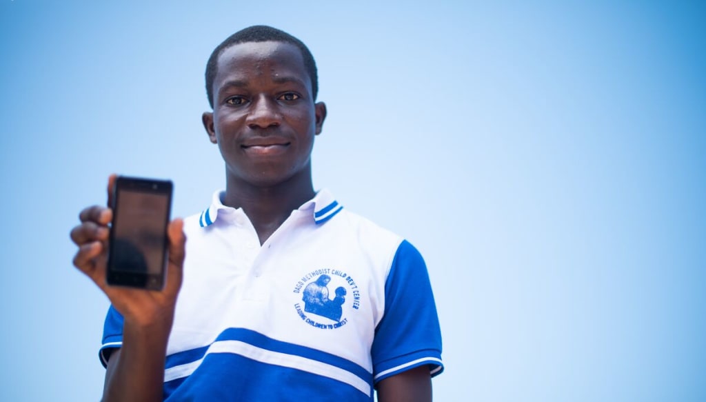 Young man wearing a blue and white collard shirt holds a cell phone facing the camera