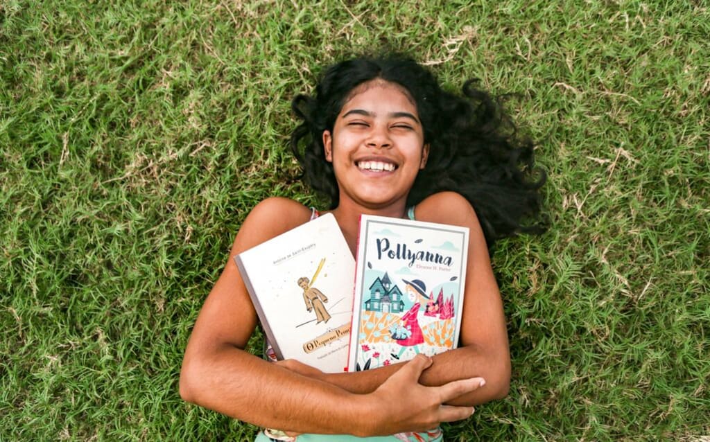 A young teen girl lies in the grass holding two books