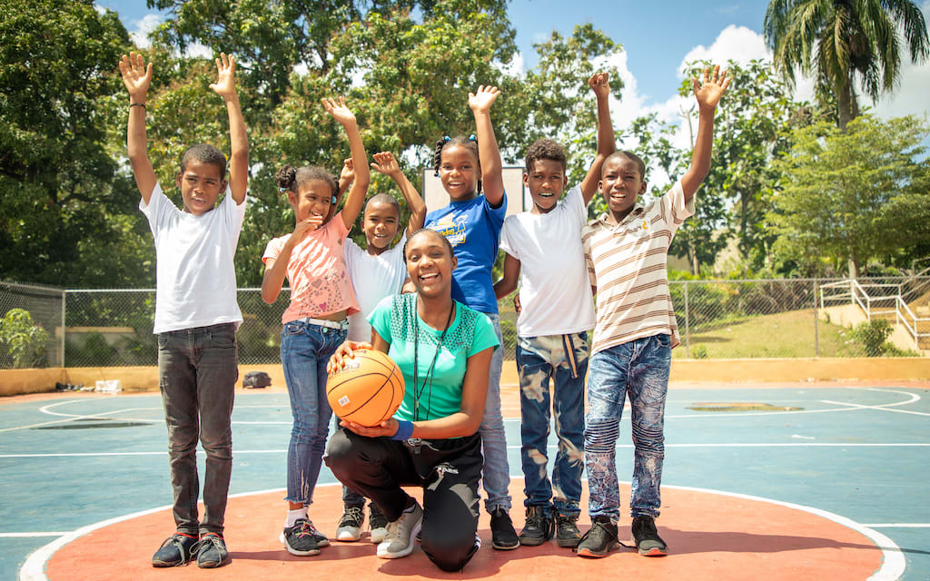 A group of kids smiles of a basketball court, with a couch in the middle smiling.