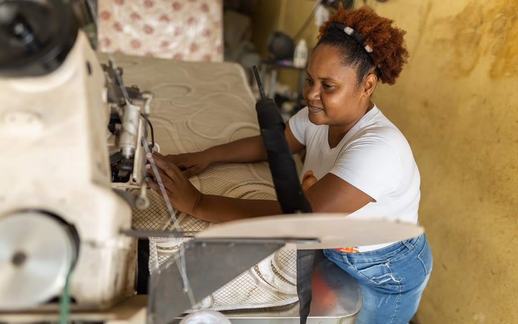 Yenny is hemming a mattress— a skill she learned through job skills training.