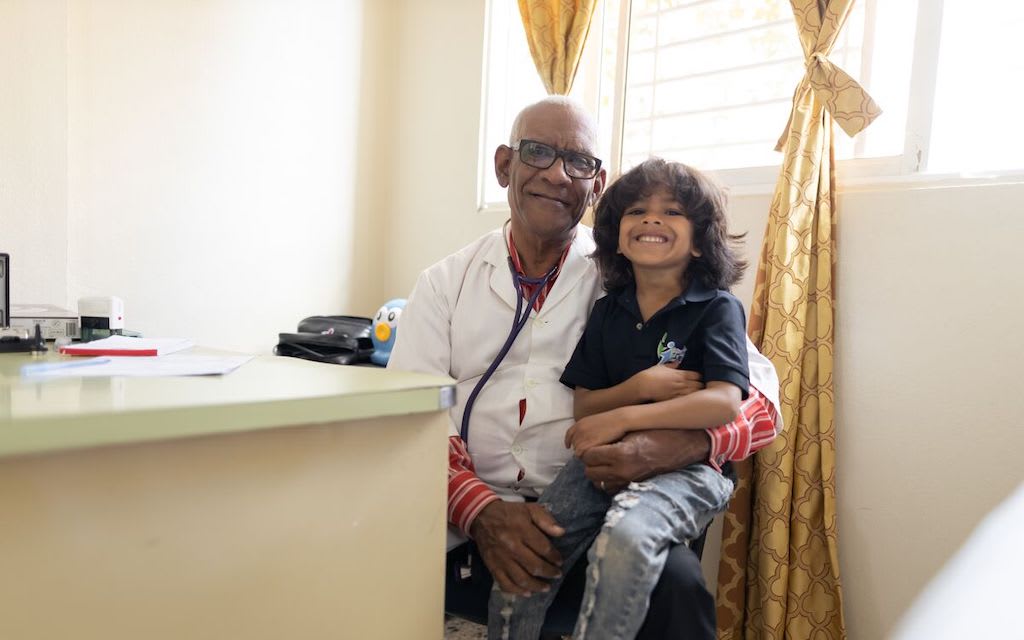 A doctor smiles with a child sitting on his lap.