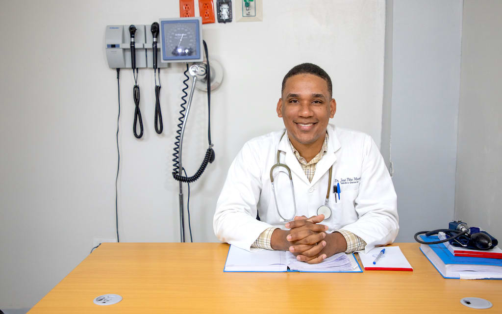 Jose sits at his desk wearing a doctor's uniform.
