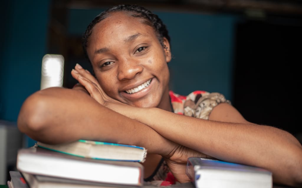 Young woman poses with her arms crossed over a stack of books, displaying her bright smile as she prepares to graduate from the Compassion program