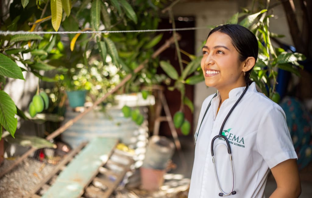 A young woman stands in her medical uniform with a stethoscope around her neck. Genesis will work in the medical field and continue to perform as a musician as she graduates the Compassion program.