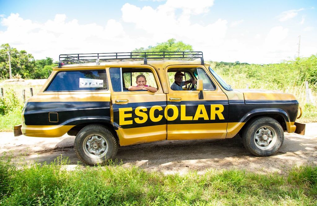 A girl sits in a yellow and black car that has "Escolar" printed on the side.