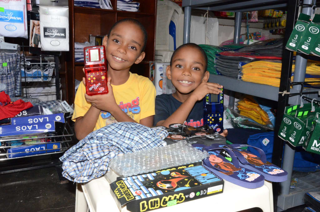 Amauris Jimenez Jimenez and Adoni Jimenez Jimenez smile together standing in a store holding toys on a table with games and clothes