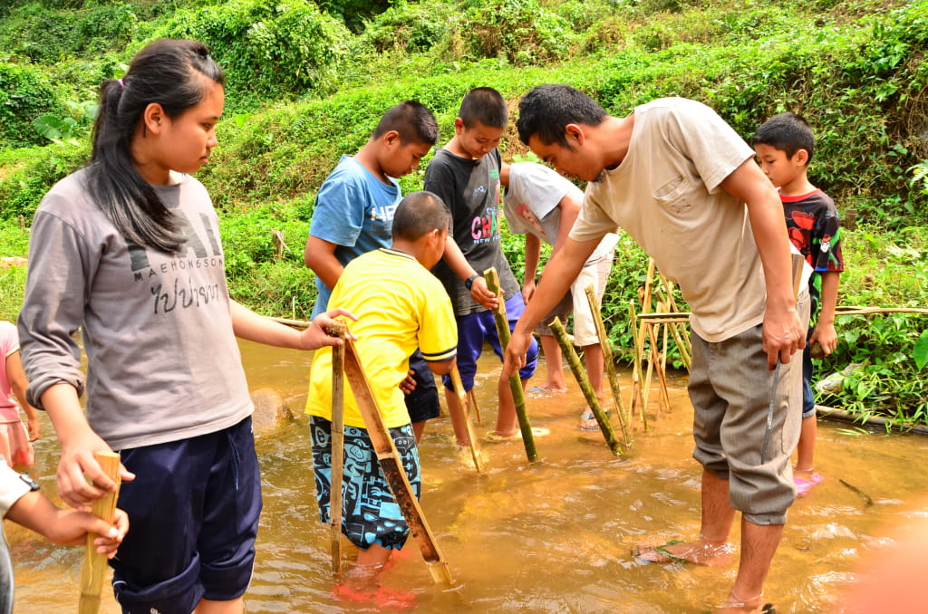 Project worker and students standing in river with Bamboo sticks in hand