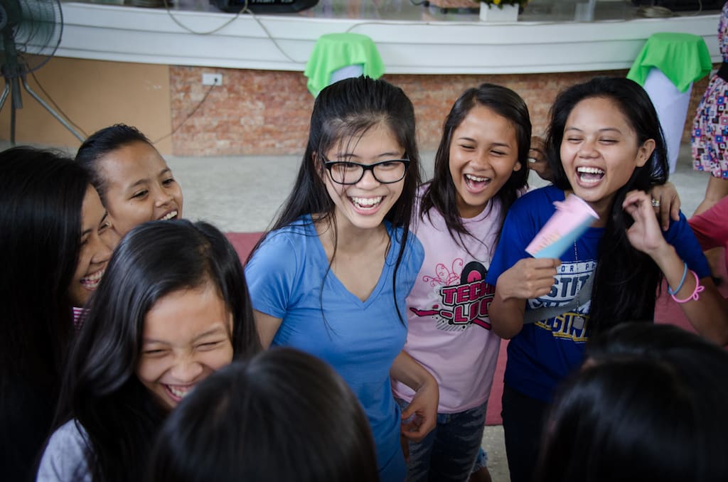 A group of girls stand in a circle, laughing and chatting.