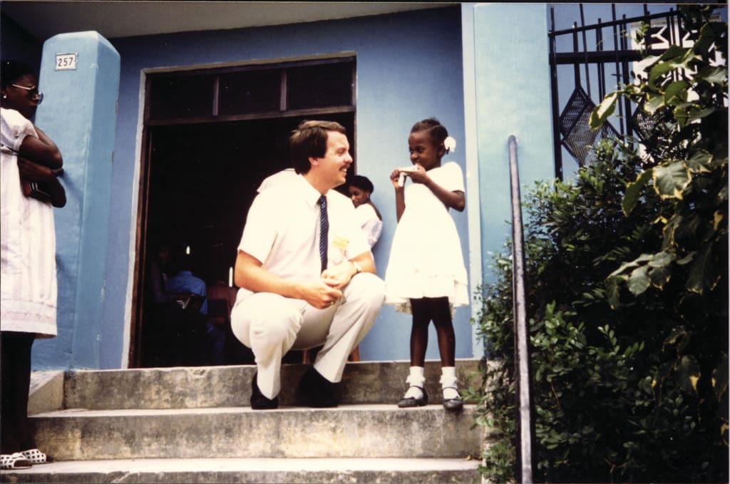 Barry Slauenwhite kneels to eye level with a Haitian girl on the steps of a church building.