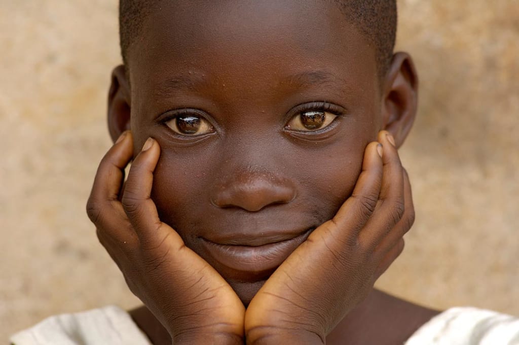 A child looks into the camera and smiles peacefully.