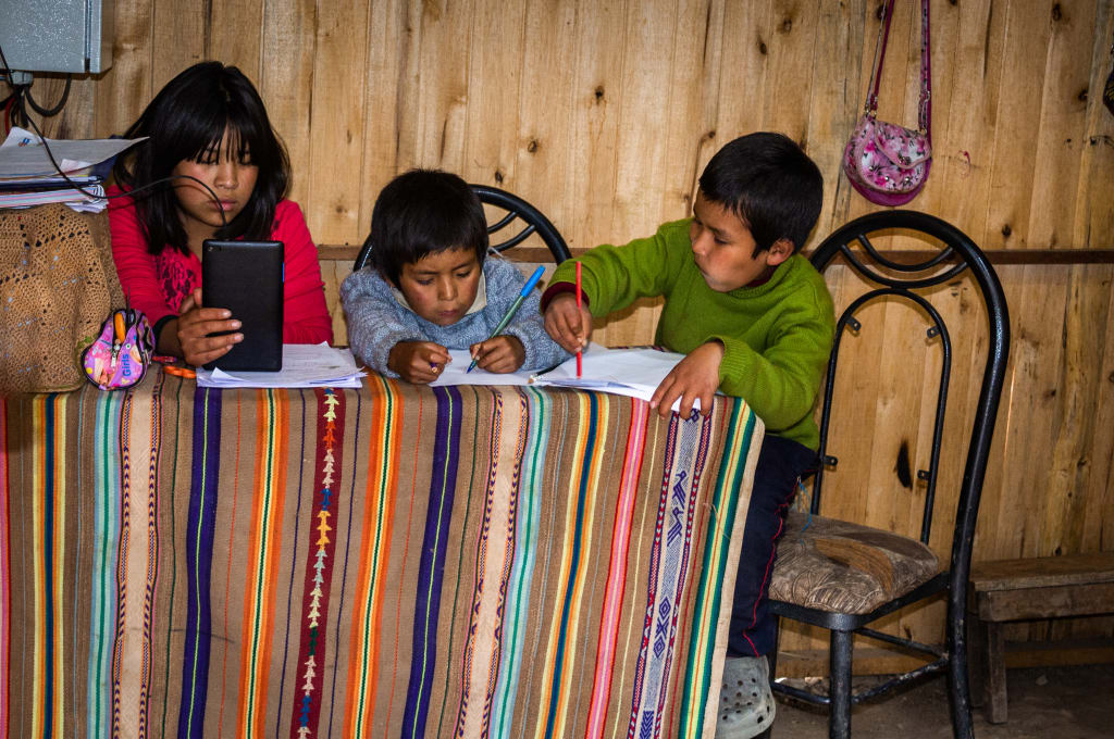 Three siblings do homework together at a kitchen table in Peru.