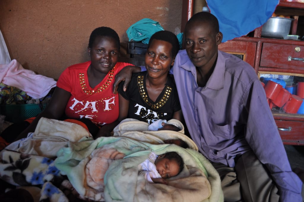 Annet is seen holding her triplets while sitting in between a man in a blue shirt and a woman in a red shirt.