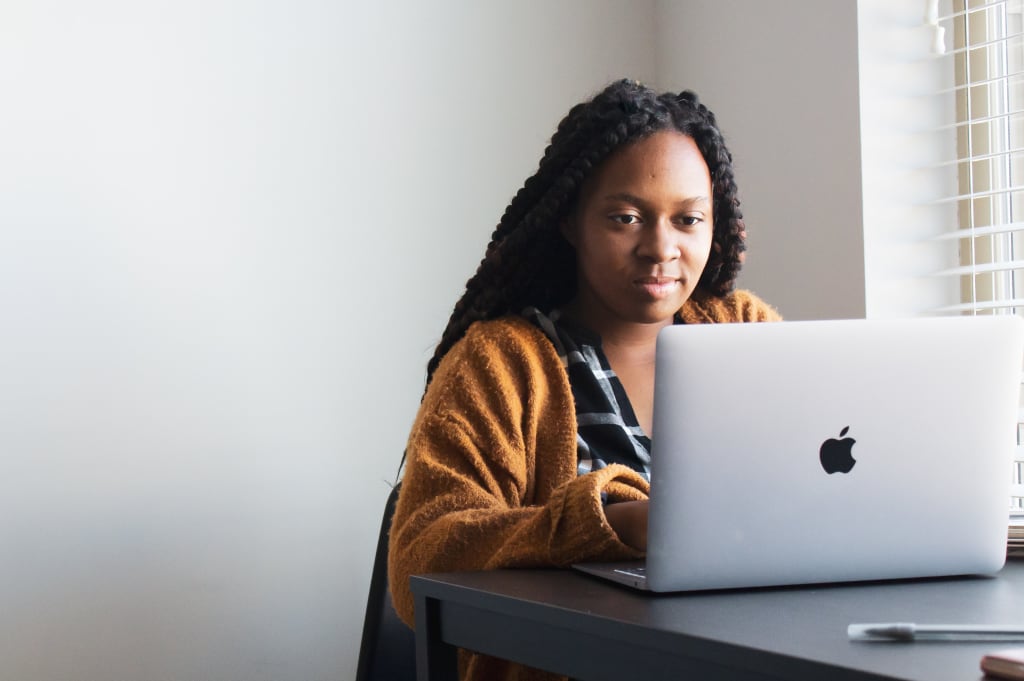 A woman in an orange cardigan looks at her laptop