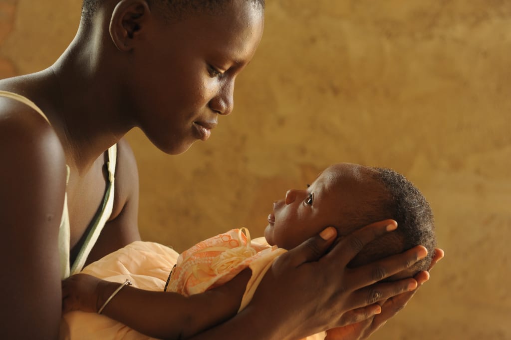 A young African mother holds her newborn baby in her arms and looks down at her