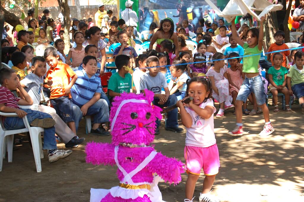 Little girl wearing pink shorts and surrounded by excited kids tries to hit the pink cat pinata