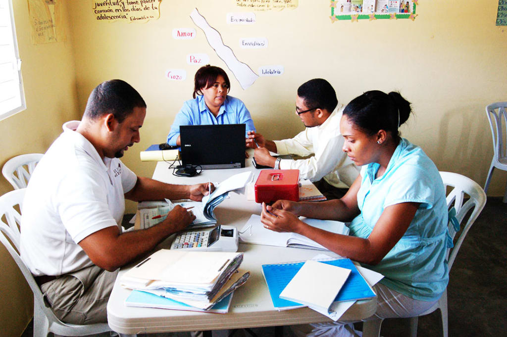 A woman sits at a table at a child centre and does paperwork with a team of two men and one other woman.