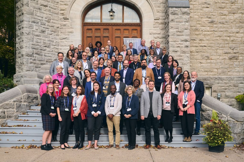 A large group of leaders stand together for a photo on the steps of a stone building.