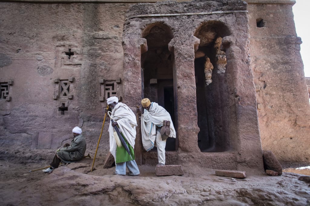 A group of Ethiopian Orthodox Priests, adult males wearing white robes walk through The Church of Saint George, one of many monolithic rock-cut churches hewn into the rocky hills of Lalibela, Ethiopia.