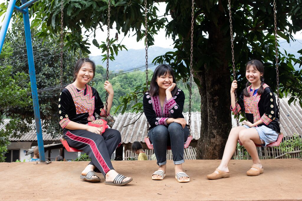 Three girls sit on a swing set.