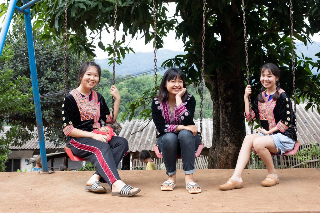 three girls sit on a swing smiling at the camera