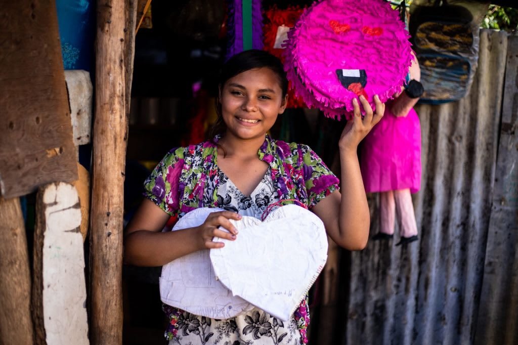 Estrella poses with an unfinished and a finished pinata she has made.