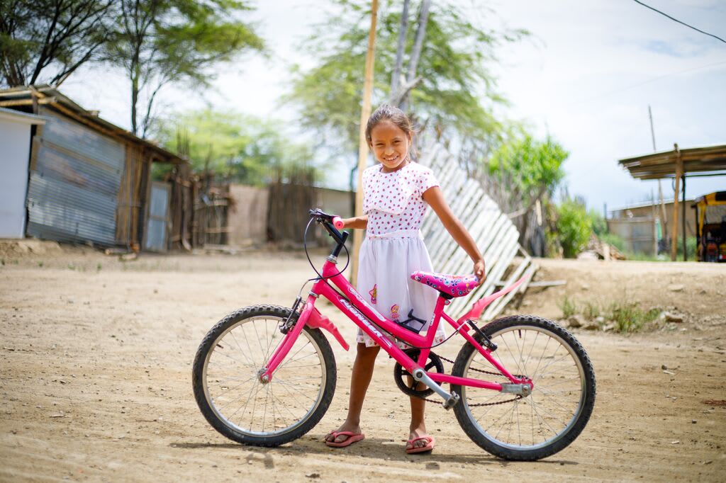 little girl holding a pink bike on a sunny day smiles