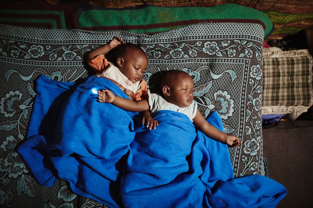 The twin baby girls sleep soundly with their arms spread wide covered in a blue blanket
