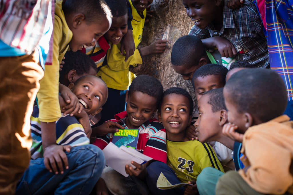 A group of young boys crowd around eachother, smiling and laughing as they read eachother's sponsor letters.