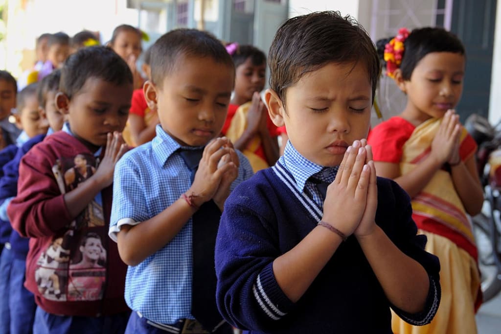 Young, Indian boys stand in class, with their hands folded to pray.