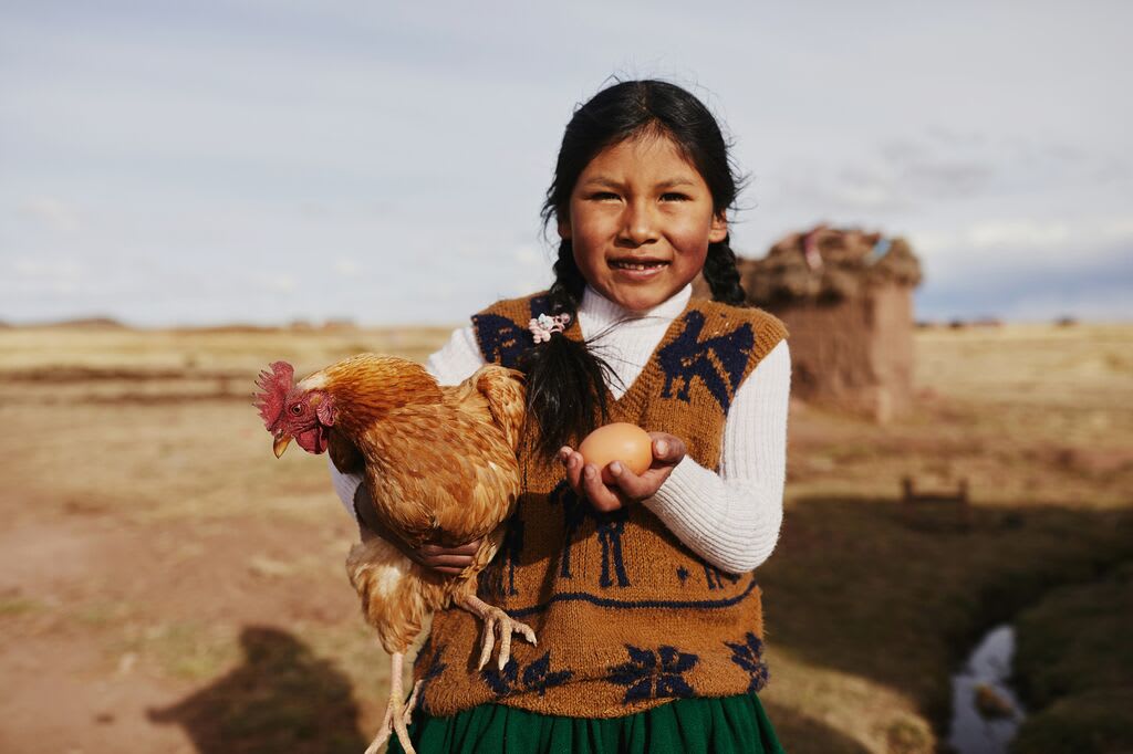 Girl holds a chicken in one hand and an egg in another