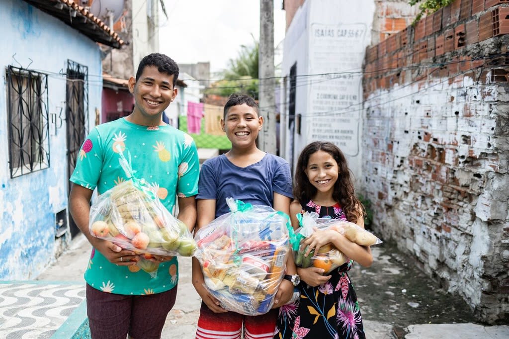 Three teenagers stand smiling with bundles of food in their arms.