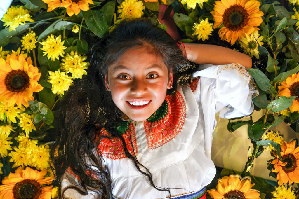 A girl in a white shirt lays amongst sunflowers.