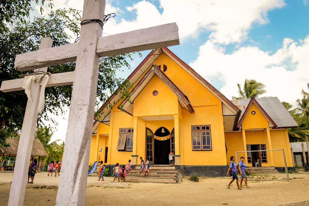 Children run into a yellow church building that has two wooden crosses standing in front.