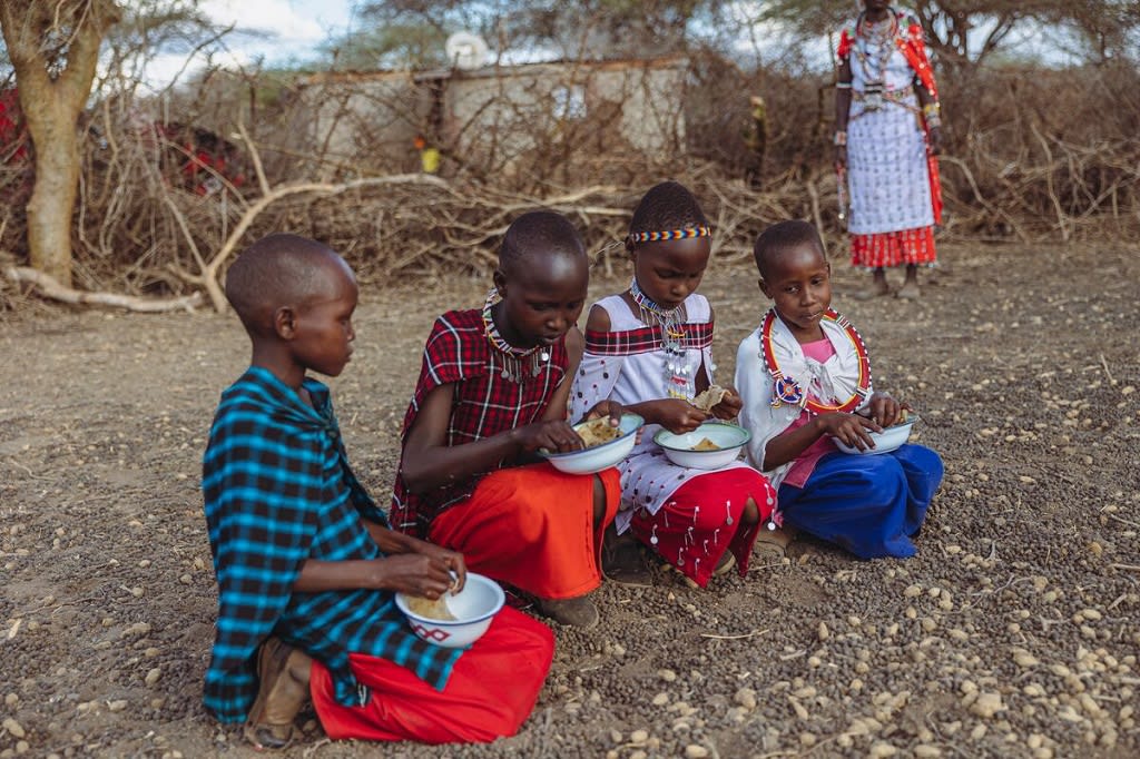 Four children sit on the ground in their traditional clothing eating a special Christmas meal.