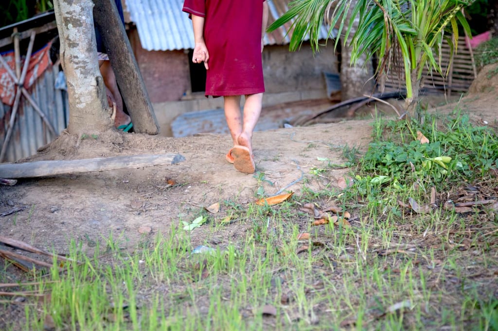 Little girl wearing a red dress and flip flops walks away from camera near her home.