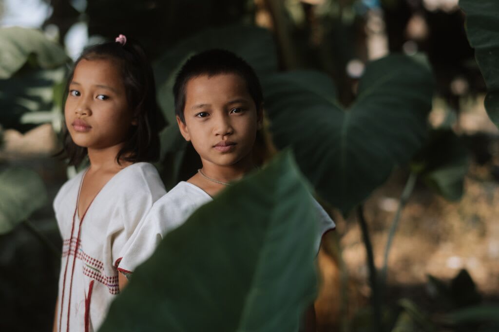 Two children standing amongst greenery.